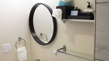 A bathroom with a white sink, a toilet, a round mirror, and a shelf with toiletries.