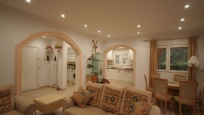 A living room with a sofa and chairs, a dining table, and a kitchen visible through an archway. - Villa Steps from the Sea (Denia)