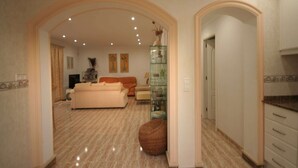 A spacious living room with a large sofa, a coffee table, and a glass cabinet. There is a door leading to another room. - Villa Steps from the Sea (Denia)