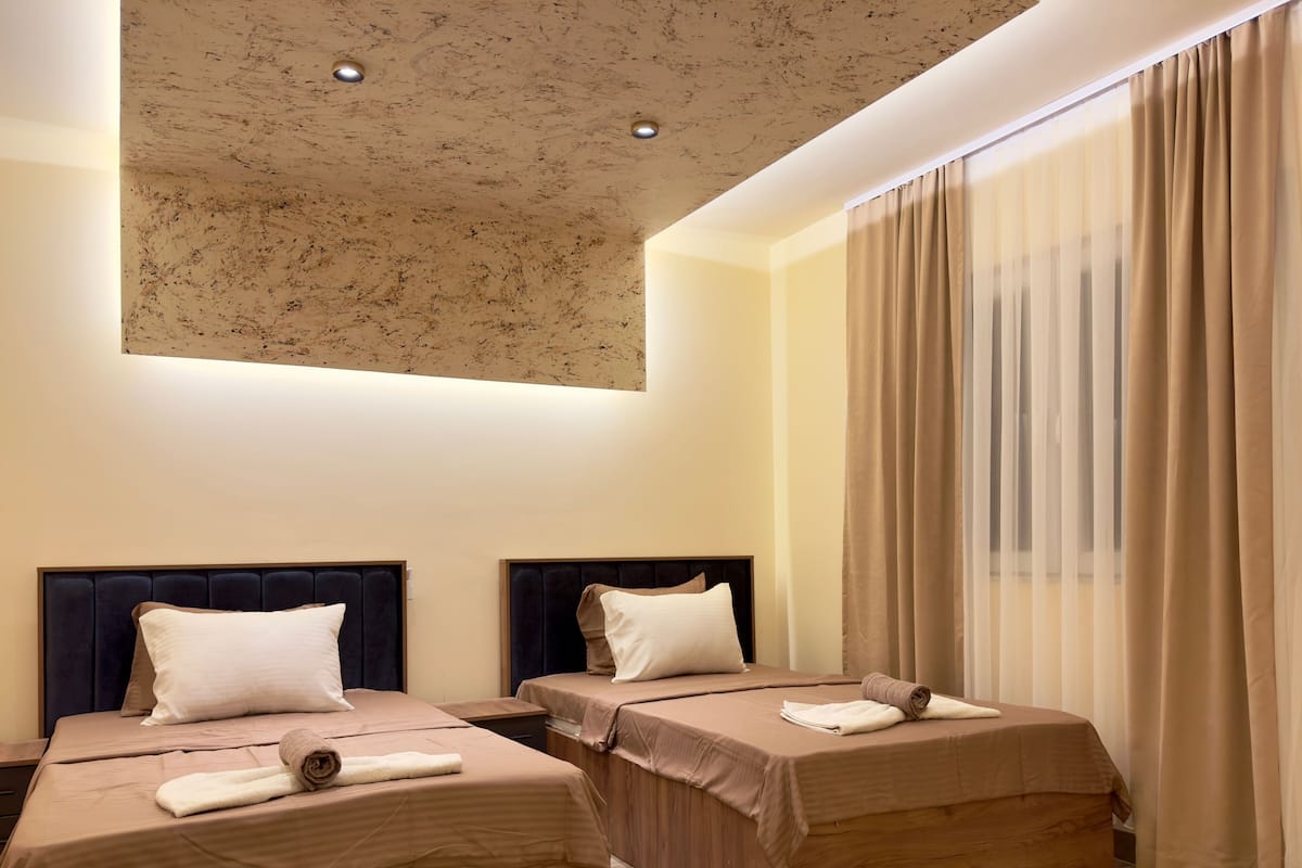 Ein Hotelzimmer mit zwei Betten, einer Deckenleuchte und einem großen Fenster mit Vorhängen.