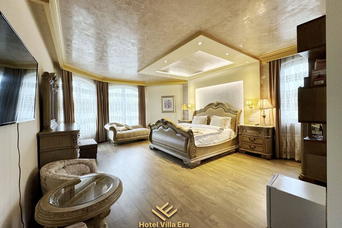 Ein geräumiges Schlafzimmer mit einem großen Bett, einer Chaiselongue, einem Glastisch und einem Fernseher.