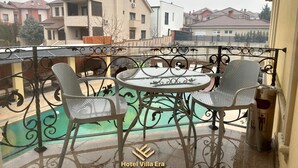 Un balcón con una mesa redonda y cuatro sillas, con vista a una piscina y edificios residenciales.