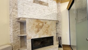 Una chimenea de piedra con estante para televisión empotrado, ubicada en una esquina de una habitación con puerta de vidrio y piso de madera.