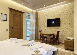 A hotel room with a bed, a desk with chairs, a TV on the wall, and a wooden door. - Hotel ERA (Pristina)