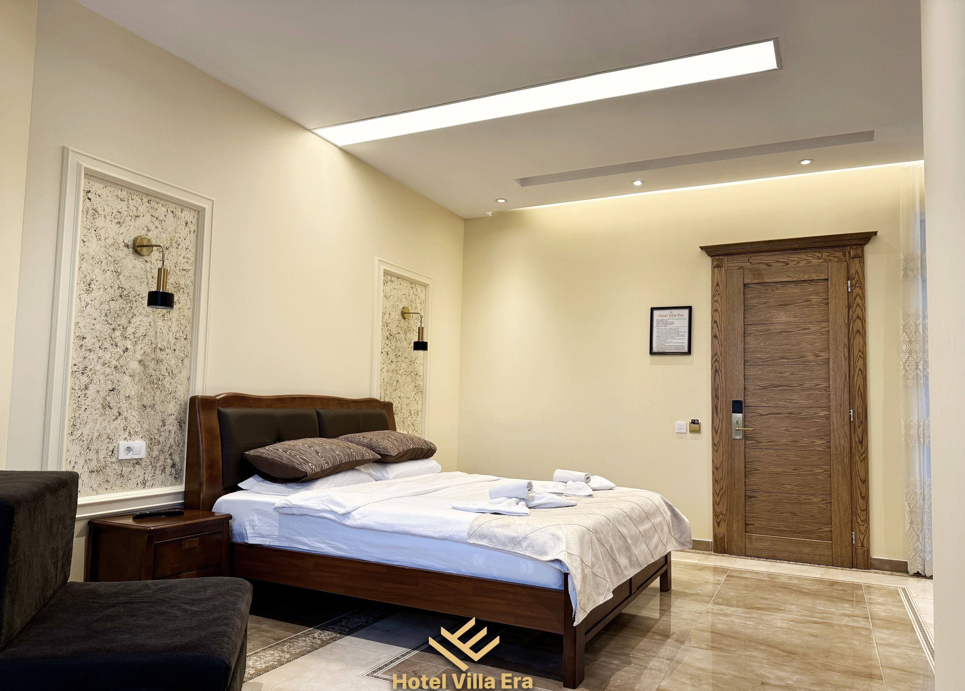 Een hotelkamer met een bed, nachtkastjes, een stoel, een deur en een wandlamp.