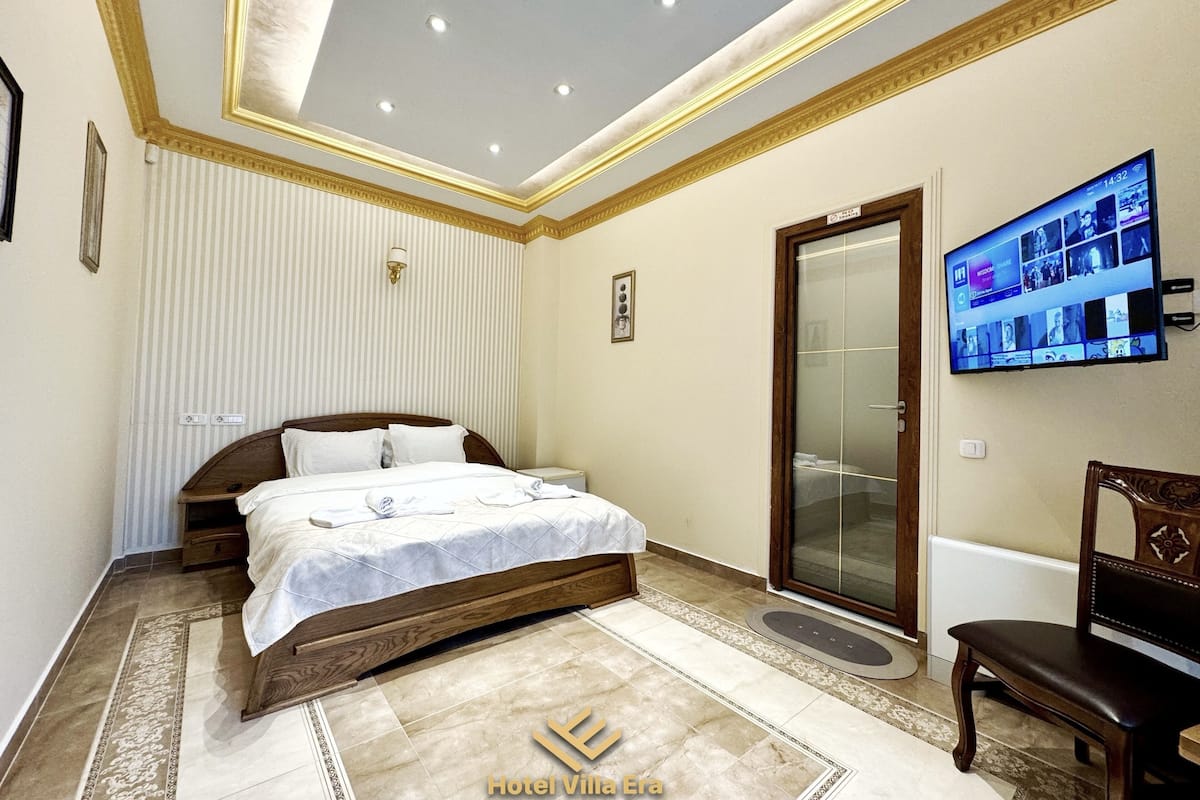 Ein Hotelzimmer mit einem Bett, einem an der Wand befestigten Fernseher, einem Holzstuhl und einer Tür zu einem Badezimmer.