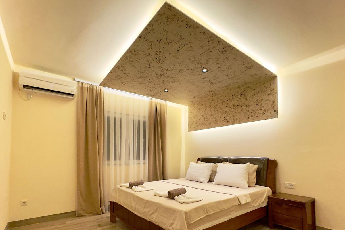 Ein Schlafzimmer mit einem Bett, einem Nachttisch, einer Klimaanlage und einer individuell gestalteten Decke.