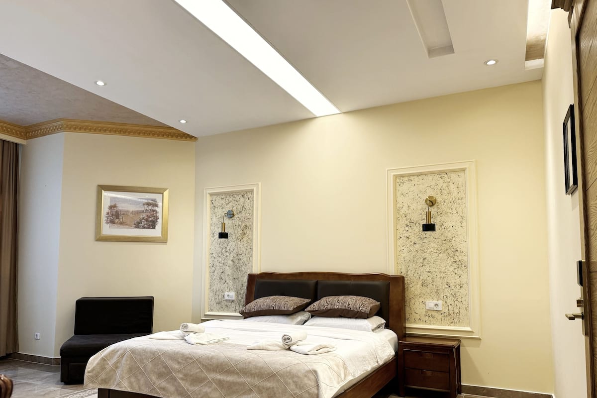 Ein Hotelzimmer mit einem großen Bett, einem kleinen Nachttisch, einem Sessel und einem gerahmten Bild an der Wand.