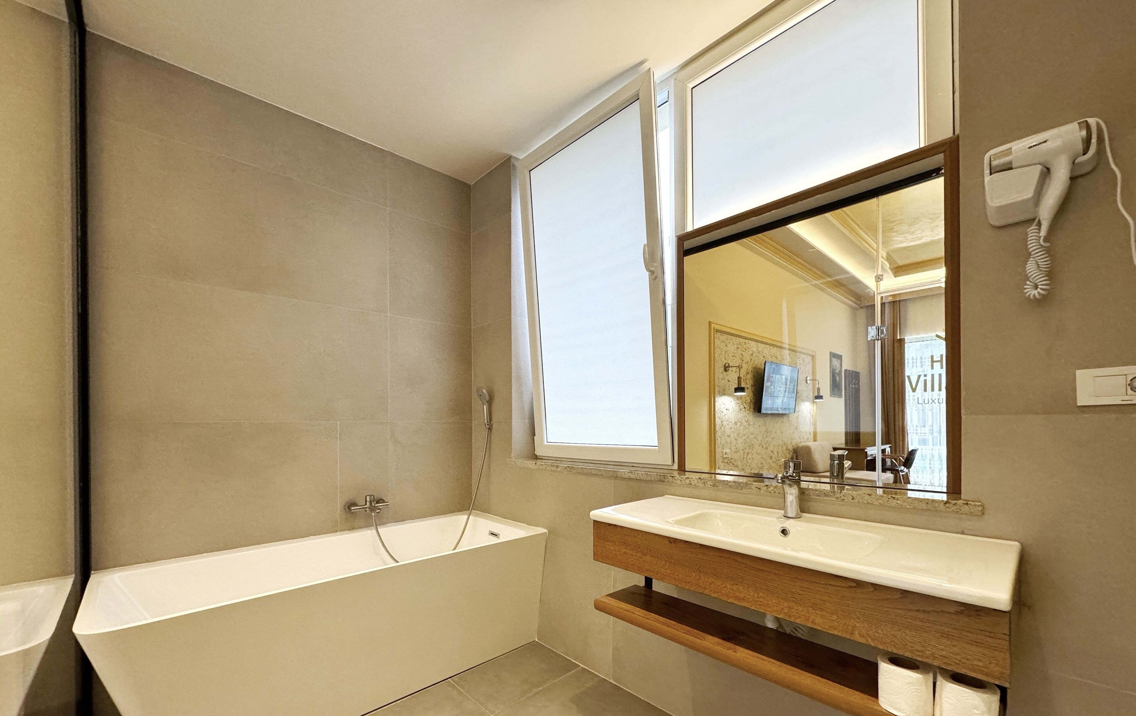 Un baño moderno con una bañera independiente, un tocador con espejo y un secador de pelo en la pared.