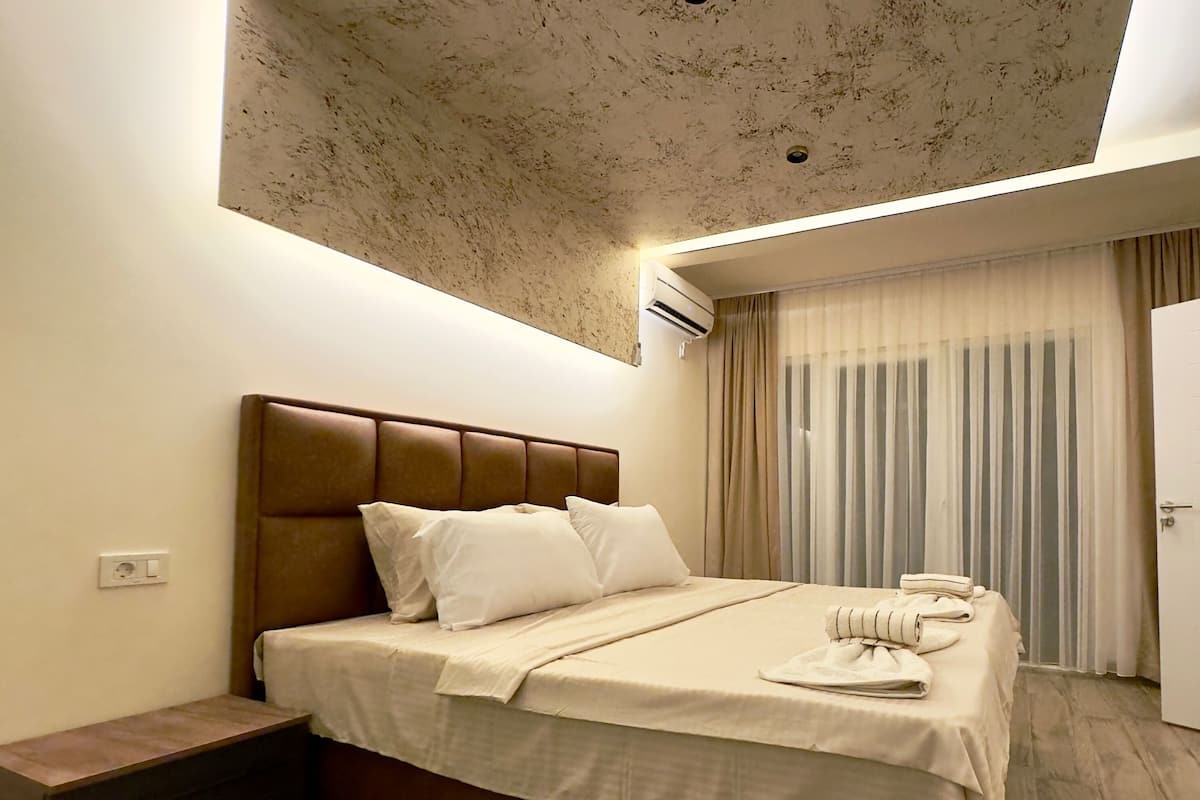 Ein Hotelzimmer mit Bett, Kopfteil, Nachttisch, Kleiderschrank und Deckenleuchte.