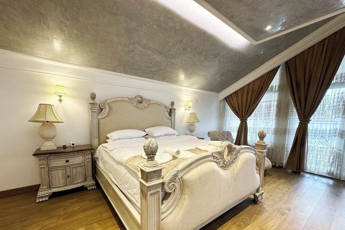 Un dormitorio amplio con una cama grande, un cabecero decorado y vistas a la ciudad a través de amplias ventanas.