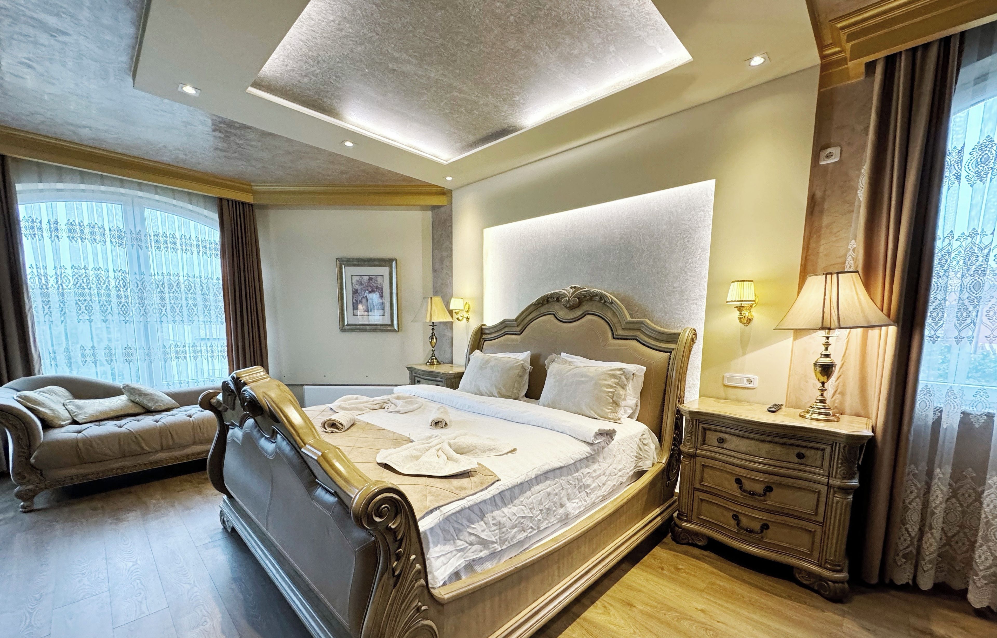 Quarto de hotel bem equipado, com uma cama grande, um sofá, uma mesa de cabeceira com abajures e um lustre no teto.