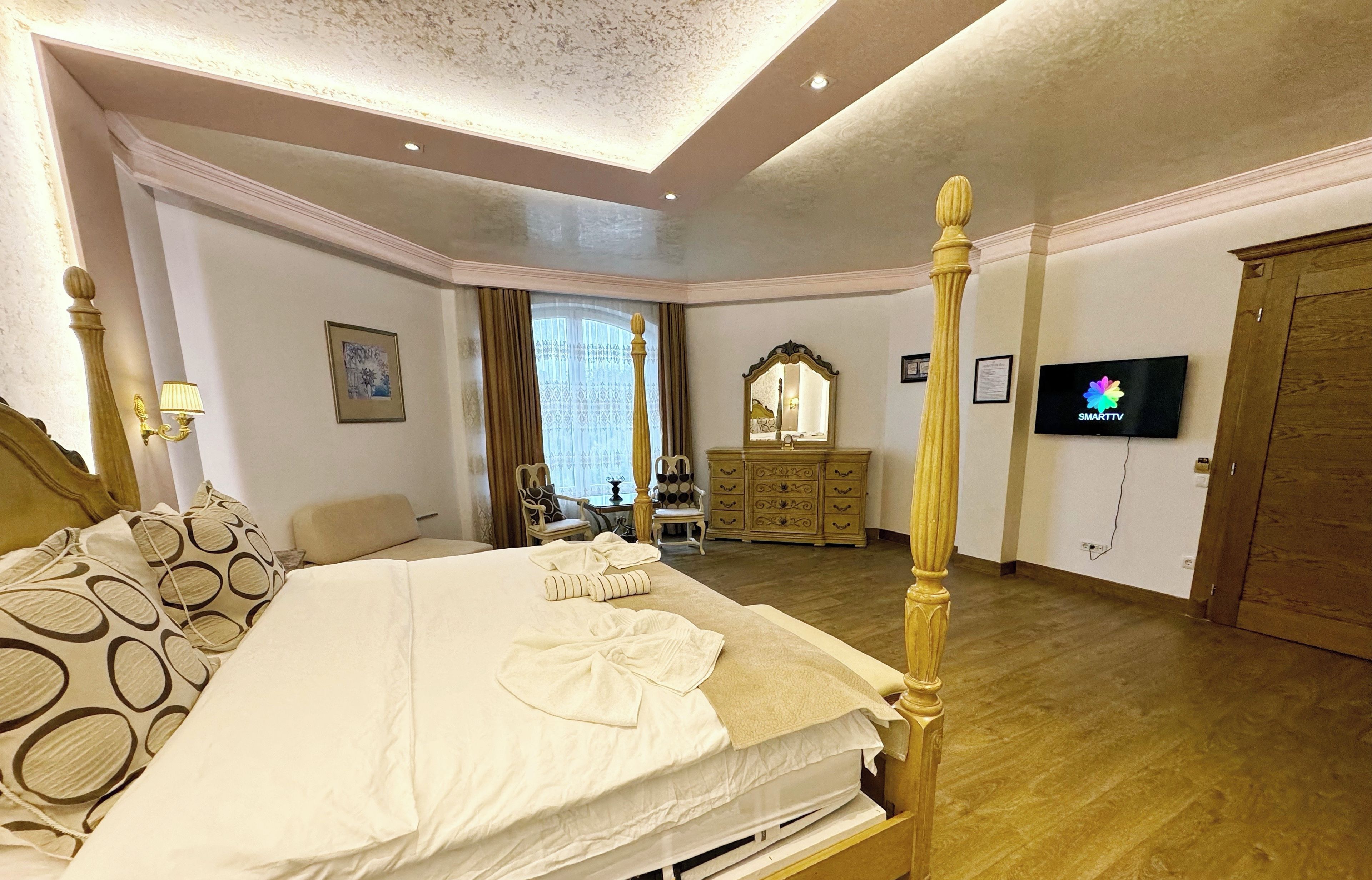 A well-appointed hotel room with a large bed, a wooden four-poster headboard, a television, and a wooden wardrobe.