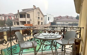 Un balcón con una mesa redonda y cuatro sillas, con vista a una piscina y edificios residenciales.