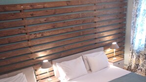 A hotel room with two beds, wooden headboard, bedside lamps, and a window with curtains. - Litsas House Platanias (Skiathos)