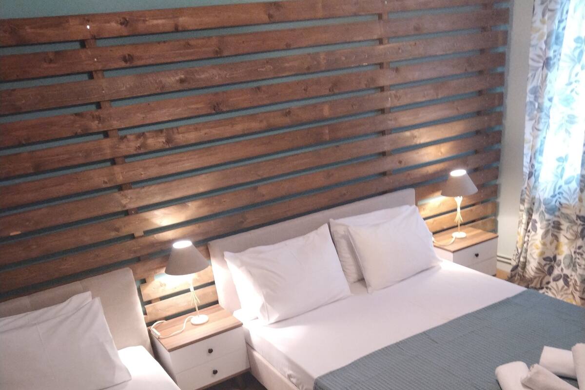 A hotel room with two beds, wooden headboard, bedside lamps, and a window with curtains.