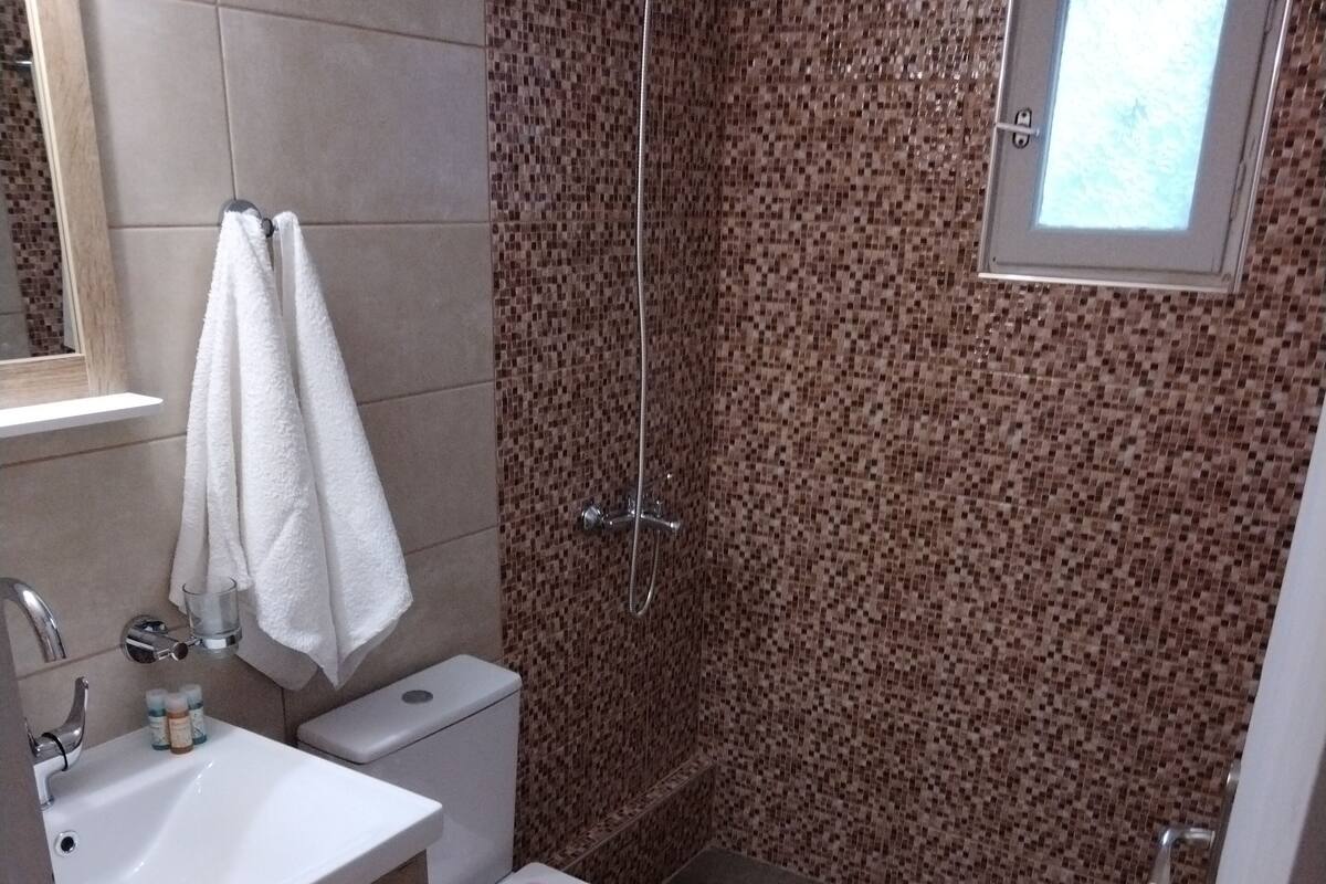 A bathroom with a shower, toilet, sink, and a small window.
