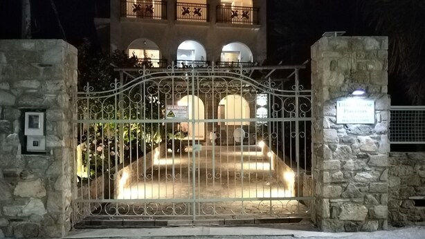 A gated entrance to a building with a stone facade, multiple balconies, and a sign indicating the name and address. - Litsas House Platanias (Skiathos)