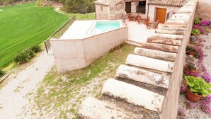 Un escalier en pierre mène à un espace piscine d’où l’on peut admirer un champ verdoyant et des arbres.
