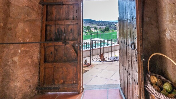 Une porte en bois rustique donnant sur un balcon d’où l’on peut admirer un paysage verdoyant et une piscine.
