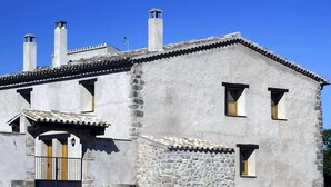 Un bâtiment en pierre avec un toit en tuiles, deux cheminées et un petit porche doté d’un portail.