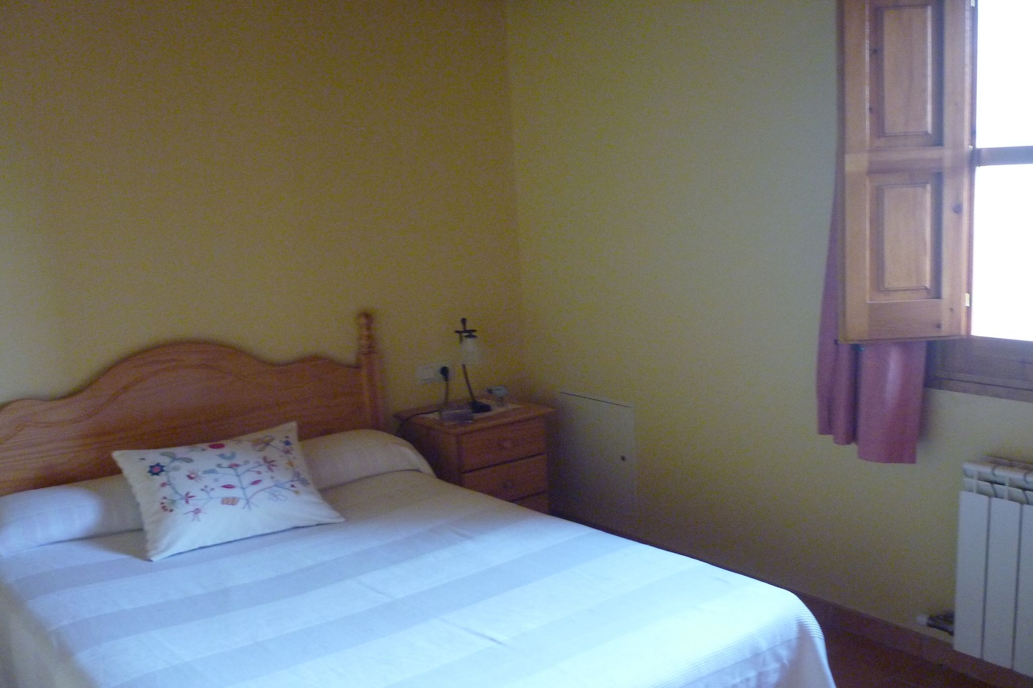 Une chambre à coucher avec un lit, une table de chevet, une lampe et une fenêtre.