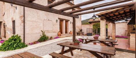 An outdoor patio with wooden tables and benches, surrounded by a stone wall and potted plants.