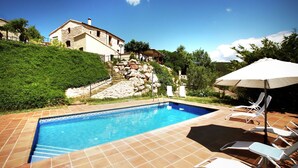 Une piscine dont le fond est recouvert de carrelage, avec un mur en pierre et un bâtiment visible au loin.