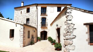 Un bâtiment à deux étages, doté d’une façade en pierre, d’un toit recouvert de tuiles et d’une entrée centrale avec une porte et des fenêtres.