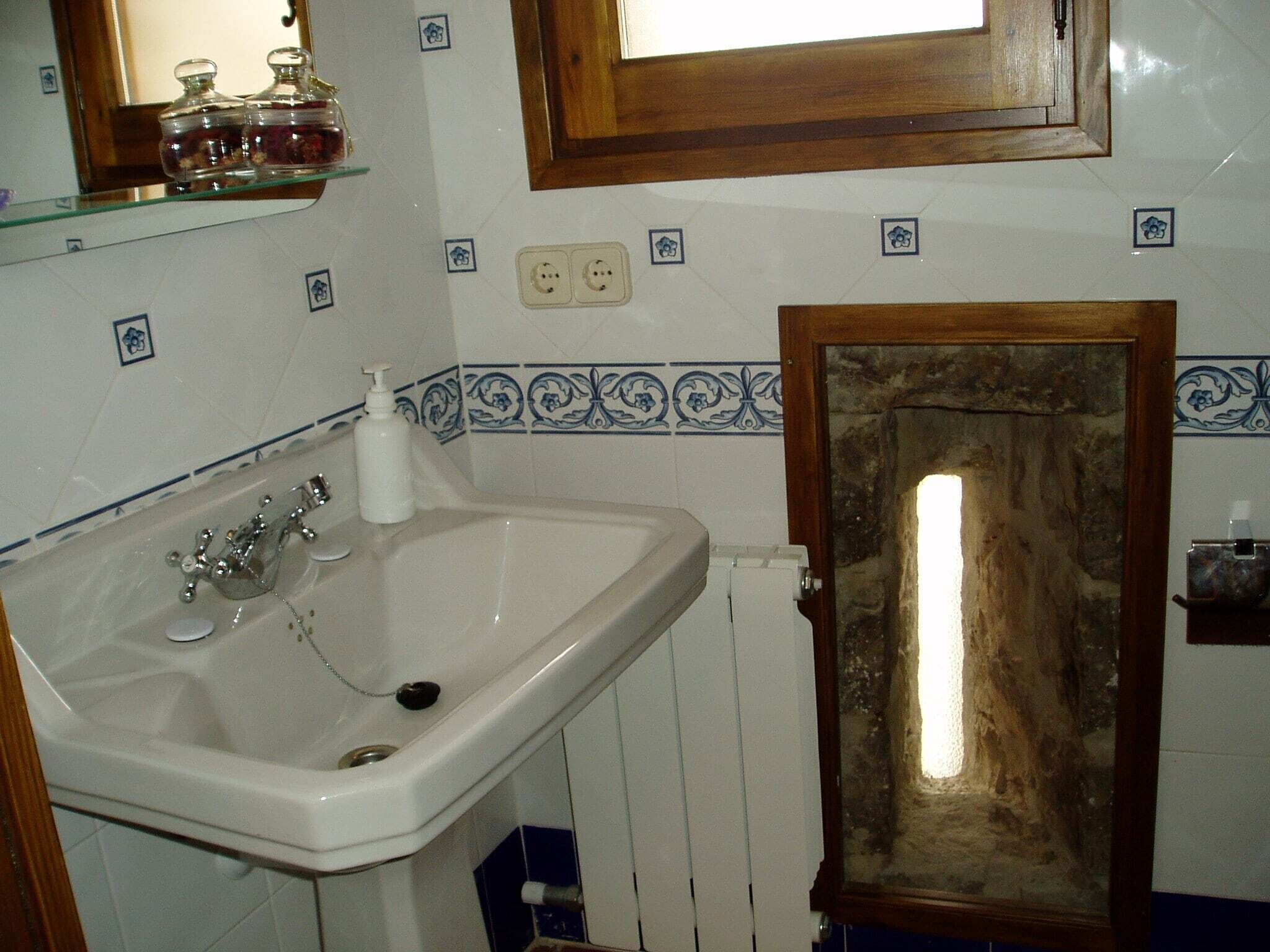 Une salle de bain avec un lavabo blanc, un miroir au-dessus, et une porte en bois à l’aspect pierre.