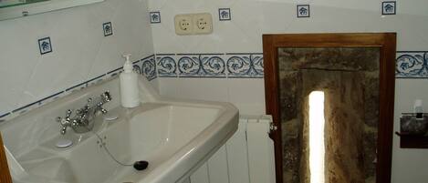 Une salle de bain avec un lavabo blanc, un miroir au-dessus, et une porte en bois à l’aspect pierre.