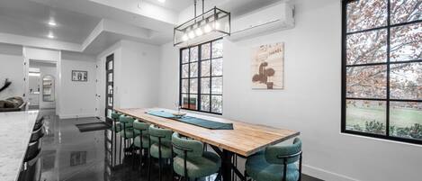 A modern kitchen with a large island, a dining area with a long table and chairs, and a large window with a view of trees.
