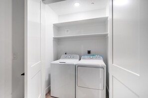 A laundry room with two white washing machines and a shelf above them. - Spacious Brand New Home! Lots of courtyard space and fun for all. (Hurricane)