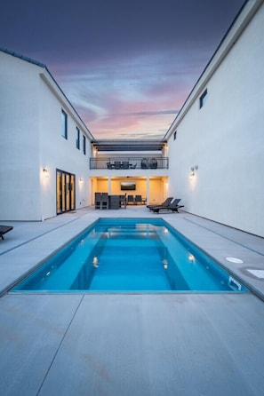 A modern pool area with a clear blue pool, a covered seating area, and a two-story building with balconies. - Spacious Brand New Home! Lots of courtyard space and fun for all. (Hurricane)