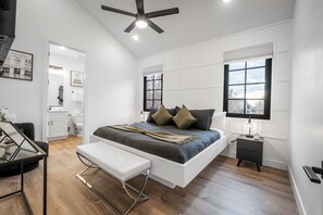 A modern bedroom with a bed, bedside table, bench, and a ceiling fan. - Spacious Brand New Home! Lots of courtyard space and fun for all. (Hurricane)