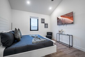 A modern bedroom with a bed, a window, a wall-mounted TV, and a console table.