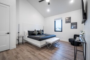 Quarto moderno com cama, mesa de cabeceira, banquinho e janela com vista.