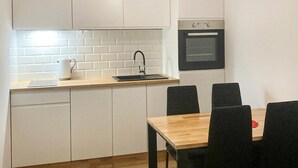 Una cocina compacta con armarios blancos, una encimera de madera, un lavamanos negro y un horno pequeño. Hay una mesa de comedor con cuatro sillas.