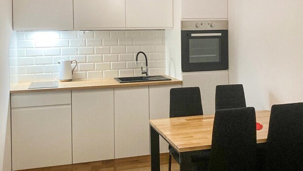 A compact kitchen with white cabinets, a wooden countertop, a black sink, and a small oven. There is a dining table with four chairs. - 1 bedroom cozy apartment in Grzybowo (Grzybowo)