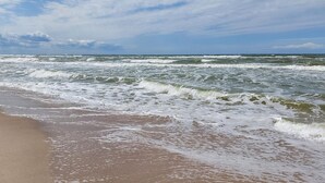 A beach with waves crashing onto the shore under a partly cloudy sky. - 1 bedroom cozy apartment in Grzybowo (Grzybowo)