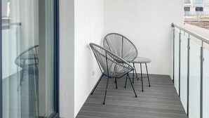 Un balcón con puerta de cristal, dos sillas de mimbre y una mesa redonda pequeña.