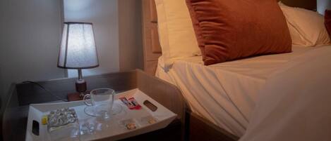 Habitación de hotel con una cama bien hecha, una mesita de noche con una lámpara y una bandeja con agua y aperitivos.
