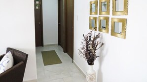 A hallway with a brown door, a white wall with multiple golden-framed mirrors, and a white vase with a plant. - Beautiful condo in La romana, DR with pool and walking distance to Caleta beach. (La Romana)