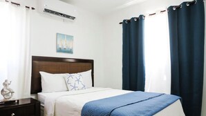 A bedroom with a bed, a nightstand, a wall-mounted air conditioner, and a painting. - Beautiful condo in La romana, DR with pool and walking distance to Caleta beach. (La Romana)