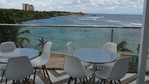 A balcony with a table and chairs overlooking a beach and ocean. - Beautiful condo in La romana, DR with pool and walking distance to Caleta beach. (La Romana)
