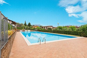 Una piscina rectangular con borde de baldosas, rodeada por un muro de piedra bajo y una cerca de metal.