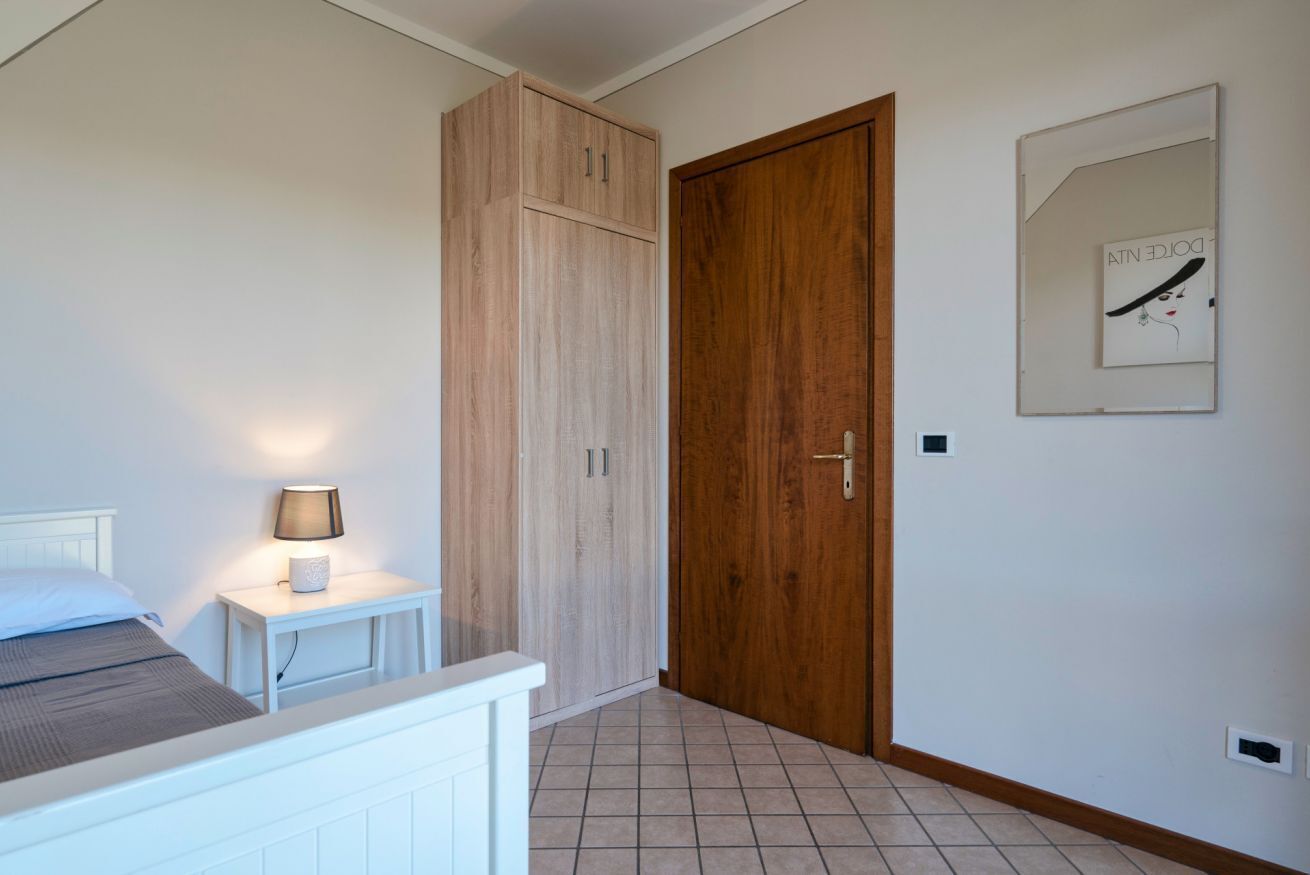 Een slaapkamer met een bed, nachtkastje met een lamp, een houten garderobe en een deur.