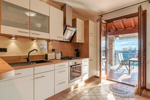Una cocina moderna con armarios blancos, una campana extractora de acero inoxidable y un amplio ventanal con vistas a un patio amoblado.