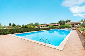 Piscina rectangular con dos escaleras metálicas a un lado, rodeada por un solárium de baldosas.