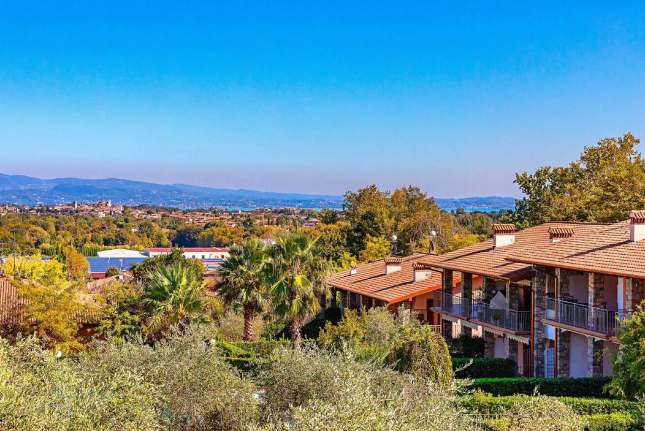A villa with a terracotta roof, surrounded by lush greenery and a view of distant hills.